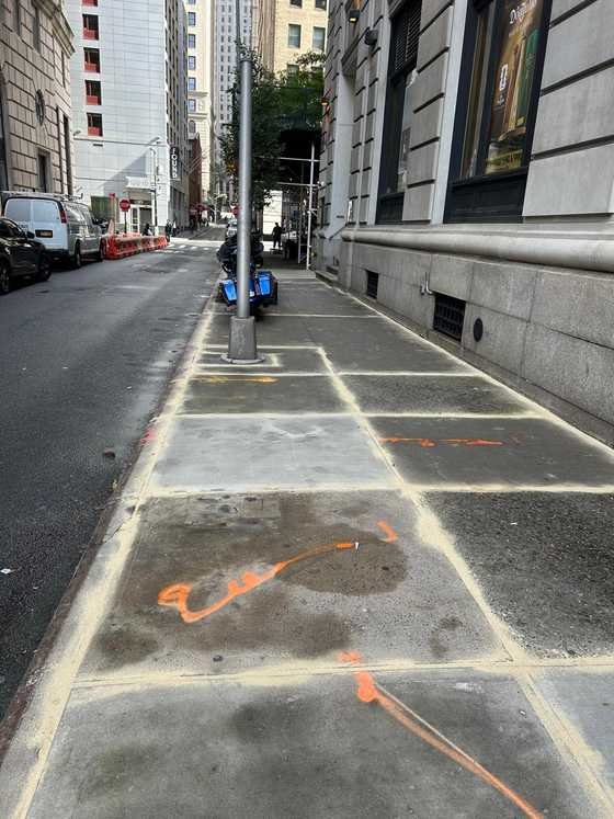 Marked sidewalk slabs along a stone building in Manhattan