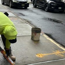 Worker applying white sealant along a new sidewalk joint in NYC