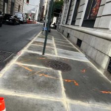 Sidewalk slabs around a manhole and sign pole with orange markings