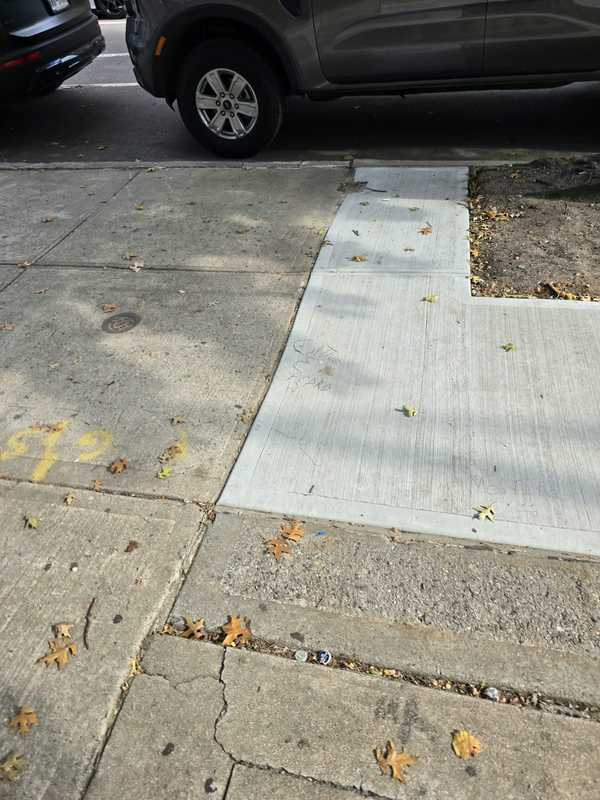 New concrete sidewalk slabs beside older pavement with a parked car nearby
