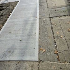Fresh concrete slabs next to cracked older sidewalk and leaf-covered pavement